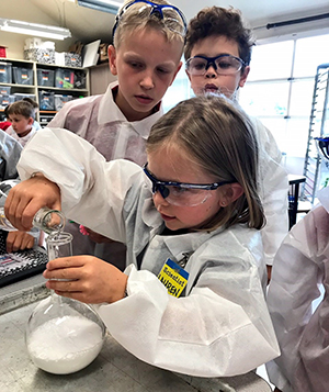 Girl pouring material into beaker in classroom